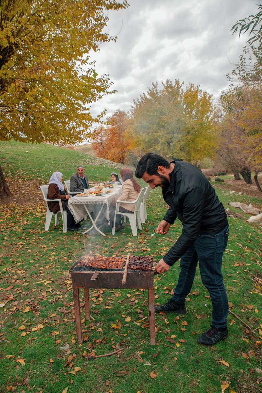 Man Grilling Meat with Family Eating Food at the Park